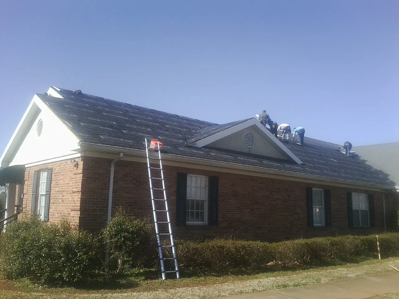 Crew tearing shingles off a brick ranch roof with a ladder set — Metal Roof Repair work by our crew in Mukilteo