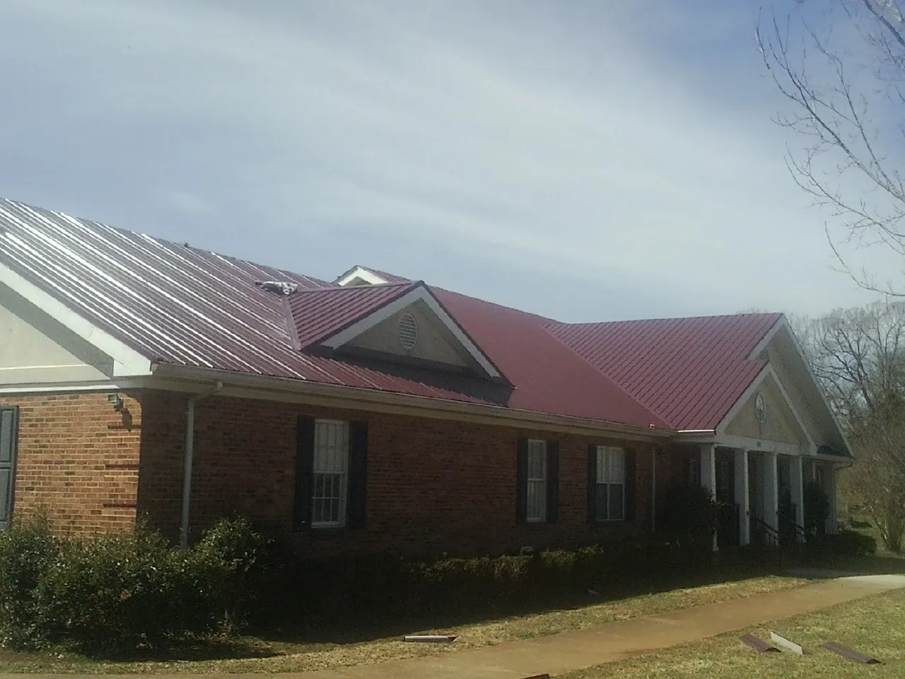 Red metal roof with gabled entries on a long brick building, from a Hail Damage Roof Repair job in Mukilteo