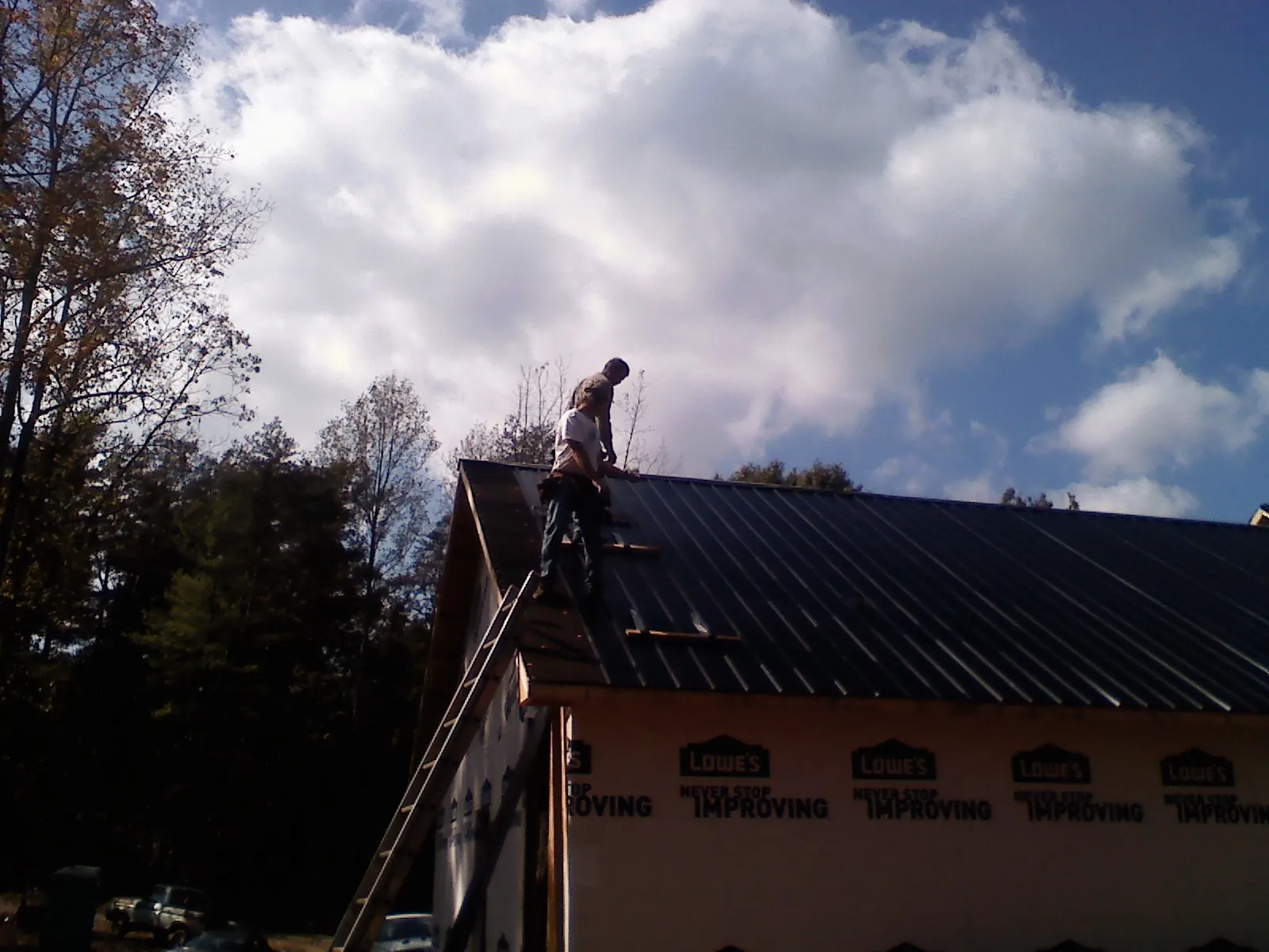 Roofer fastening dark metal panels high against a cloudy sky, from a Roof Inspection job in Mukilteo