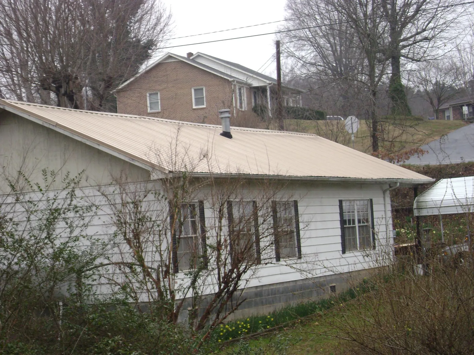 Tan metal roof on a white sided house set into a hillside — Commercial Roofing by Roofing Brothers in Mukilteo